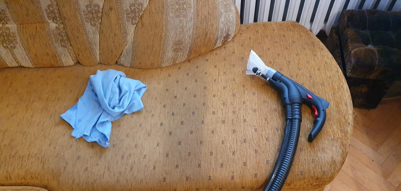Dysza odkurzacza piorącego leżąca na brązowej kanapie ze wzorem, obok niej leży złożona niebieska ściereczka z mikrofibry.