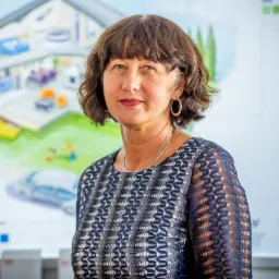 Portret kobiety z rysunkiem domu i samochodu w tle, sugerujący ubezpieczenie nieruchomości i pojazdu. Uśmiech, profesjonalny wygląd.