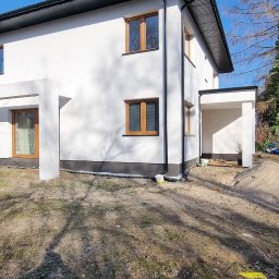 Krishome - Biały dom z brązowymi oknami w słoneczny dzień. Widoczna świeżo pomalowana elewacja i czarne rynny. Na ziemi widać resztki liści i trawy.