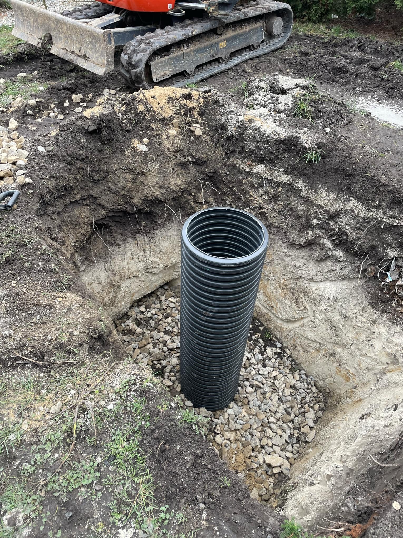 Wykopany dół z drenażem żwirowym i rurą drenarską z tworzywa sztucznego, widoczny fragment koparki.