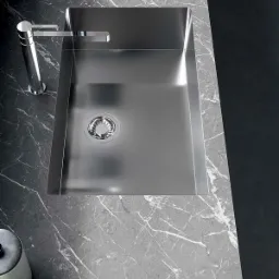 Nowoczesny, prostokątny zlew ze stali nierdzewnej z chromowaną baterią, wkomponowany w blat z szarego marmuru z białymi żyłami, widok z góry.