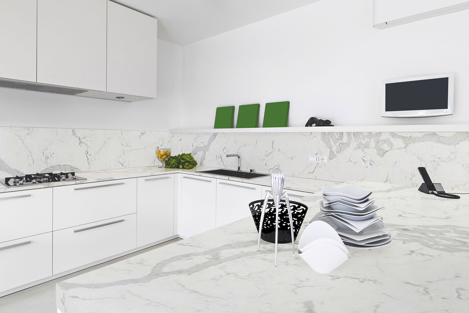 Minimalistyczna, biała kuchnia z blatem imitującym marmur, wyposażona w czarne akcenty, takie jak zlewozmywak i kosz na owoce, oraz srebrny wyciskacz do cytrusów na pierwszym planie.