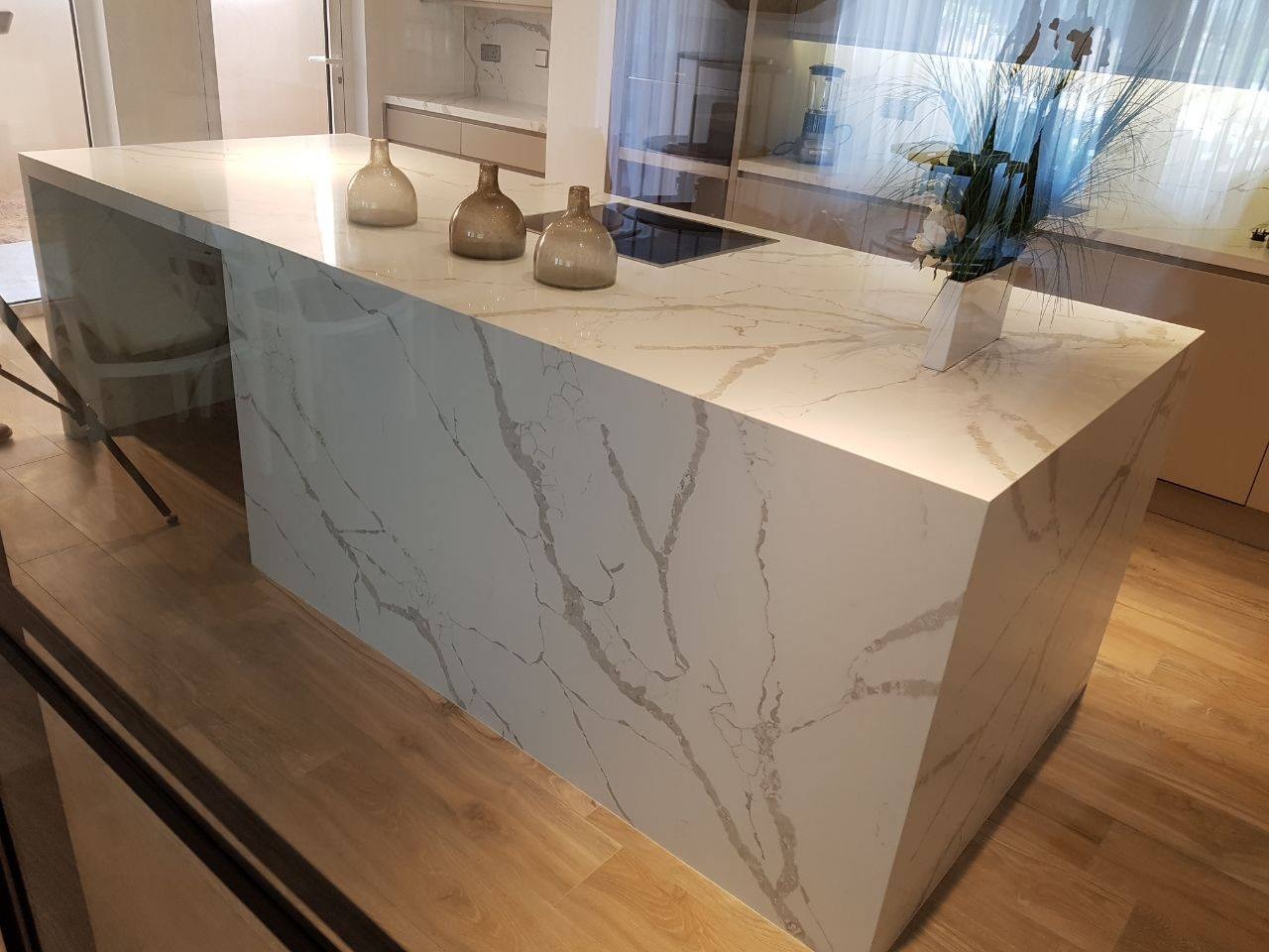 Kuchenna wyspa z blatem o wzorze imitującym marmur, z trzema ceramicznymi wazonami i minimalistycznym bukietem, na tle jasnego wnętrza.