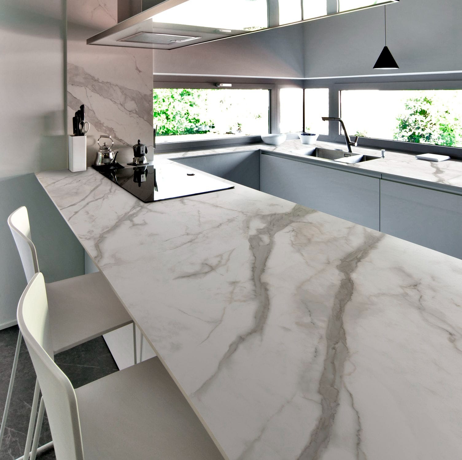 Biały blat kamienny z szarymi żyłami w nowoczesnej kuchni z oknem na zieleń, widoczne krzesła barowe.