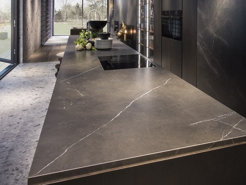 Nowoczesna kuchnia z ciemnym, matowym blatem z wyraźnym białym użyleniem, zintegrowana płyta grzewcza, widok na ogród przez duże okno.