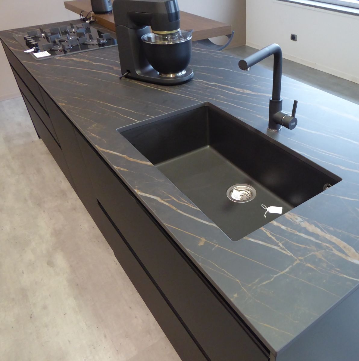 Ciemny blat kuchenny z charakterystycznym złotym żyłkowaniem, zintegrowany z czarnym zlewozmywakiem i baterią, uzupełniony o mikser kuchenny w tle.