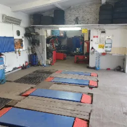 Wnętrze warsztatu samochodowego z podnośnikiem czterokolumnowym, maszynami do wyważania i montażu opon, narzędziami na ścianie i stosem opon w rogu.