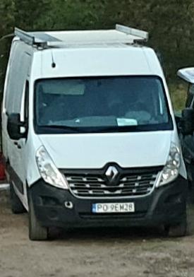 Biały samochód dostawczy Renault Master z bagażnikiem dachowym, zaparkowany na żwirowym podłożu, widok z przodu.