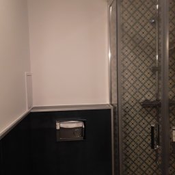 Remonty Wykonczeinie - Nowoczesna łazienka z kabiną prysznicową z wzorzystymi płytkami i czarną zabudową toalety z chromowanym przyciskiem spłukiwania.