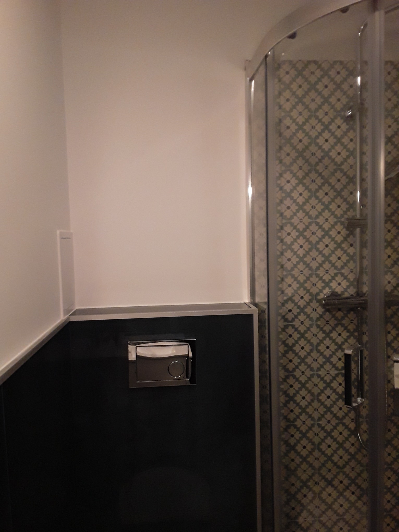 Nowoczesna łazienka z kabiną prysznicową z wzorzystymi płytkami i czarną zabudową toalety z chromowanym przyciskiem spłukiwania.