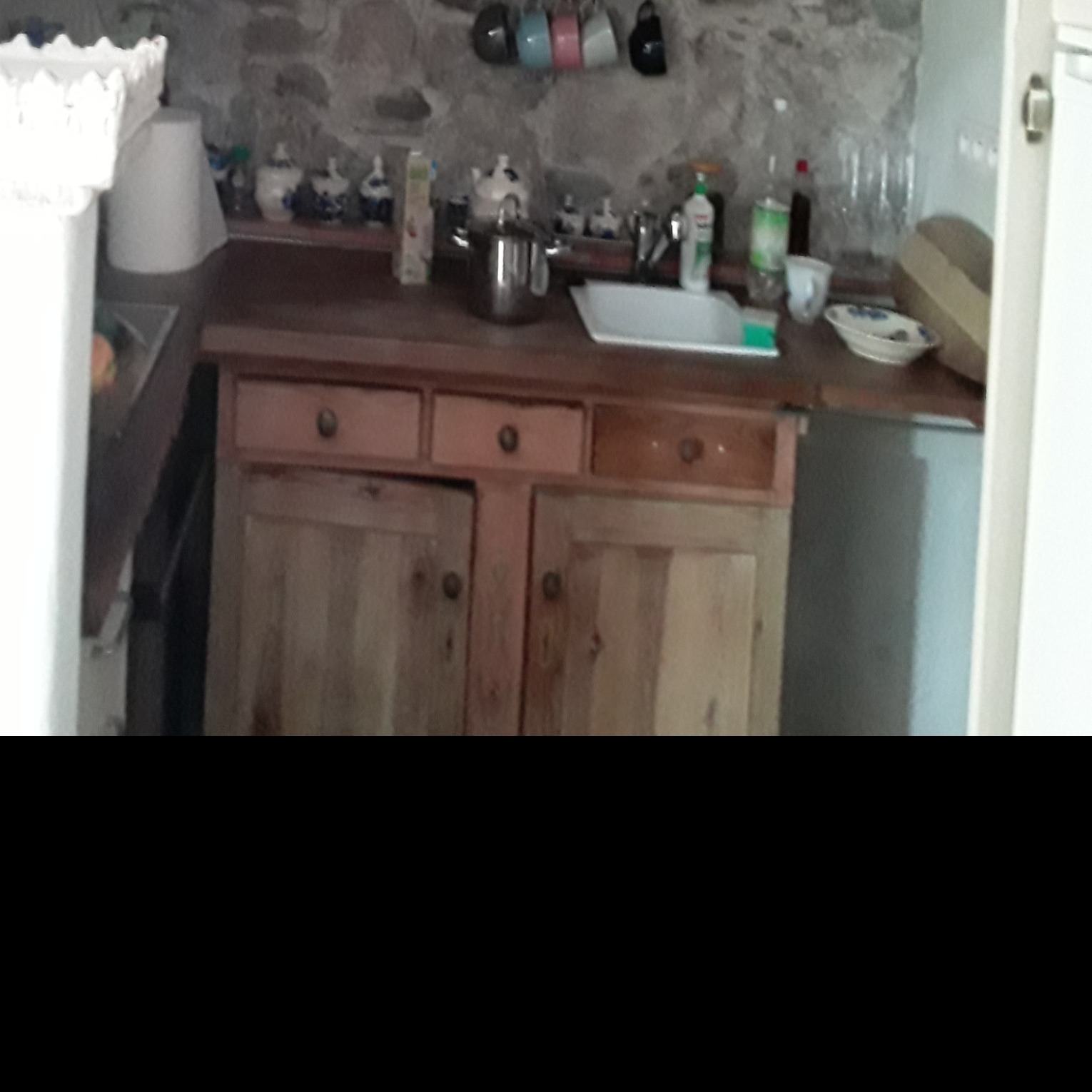 Rustykalna kuchnia z drewnianymi szafkami, kamienną ścianą i naczyniami na blacie.