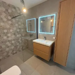 Nowoczesna łazienka z heksagonalną mozaiką pod prysznicem, drewnianą szafką z umywalką i lustrem z podświetleniem LED. Minimalistyczny design.