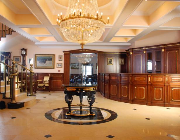 Eleganckie wnętrze hotelu z drewnianą recepcją, kryształowym żyrandolem i marmurową podłogą z dekoracyjnym wzorem.
