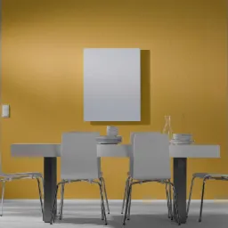 Biały panel grzewczy na złotej ścianie nad stołem jadalnym z białymi krzesłami, w tle okno z białymi szprosami.