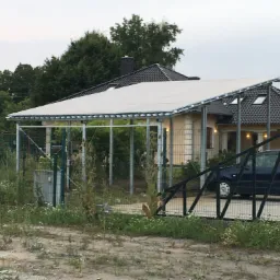 Zadaszenie tarasu z metalową konstrukcją i białym dachem, widziane zza ogrodzenia, z samochodem w tle.