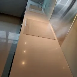 Jasny blat kamienny w kuchni z wbudowaną białą płytą indukcyjną i zlewozmywakiem, widok z góry, oświetlenie punktowe.