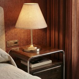 RICHTER Architekci - Stylowa sypialnia z lampką nocną na drewnianym stoliku, książka pod spodem. Beżowa pościel i zasłony w odcieniach brązu tworzą przytulną atmosferę.