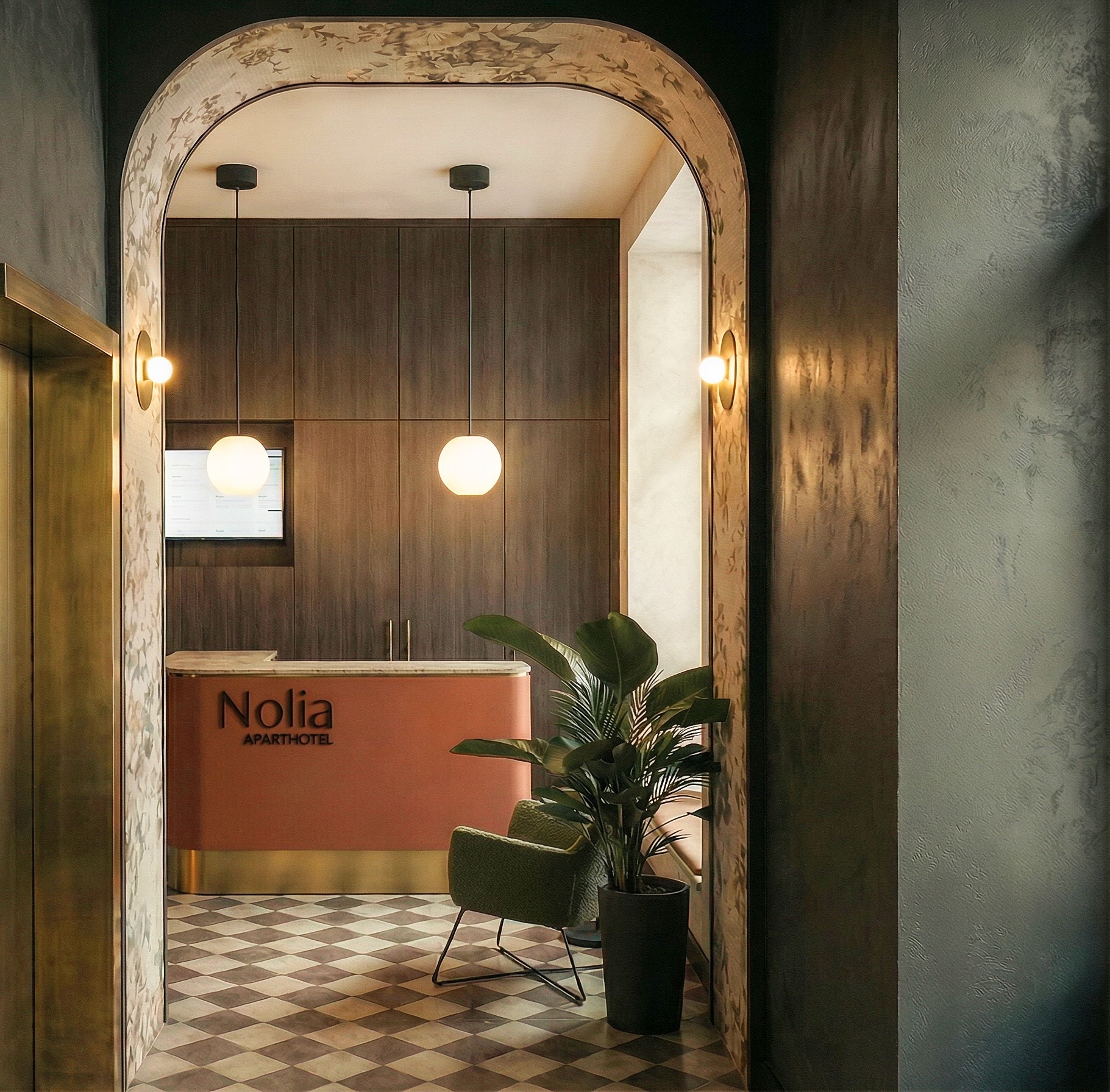 Recepcja hotelu Nolia Aparthotel z rośliną w doniczce, widoczna przez ozdobny łuk. Szachownica na podłodze, ciepłe oświetlenie i nowoczesny design.