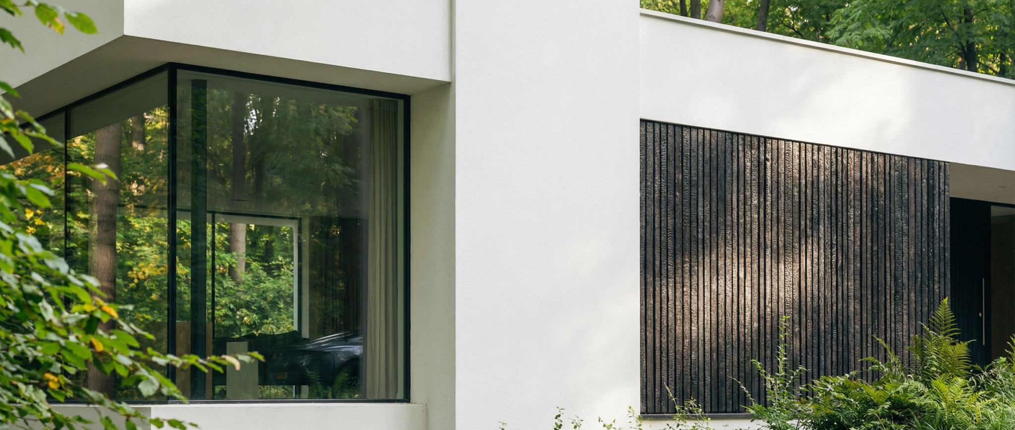 Minimalistyczna elewacja domu z dużym oknem odbijającym zieleń i panelem z ciemnego drewna. Nowoczesny design, naturalne otoczenie, geometryczne kształty.