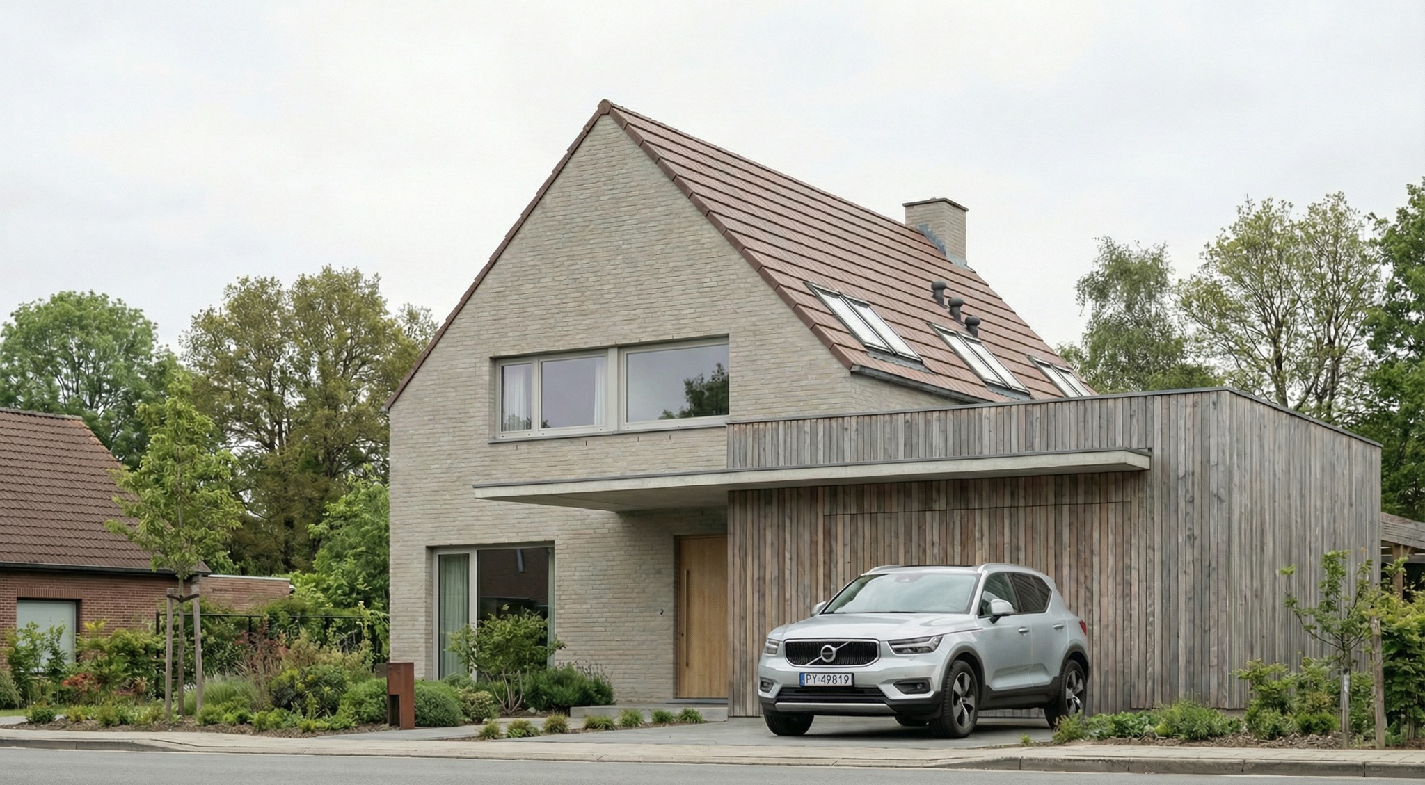 Nowoczesny dom jednorodzinny z jasnej cegły i drewnianą elewacją garażu, srebrny SUV Volvo na podjeździe, okna dachowe, minimalistyczny design.