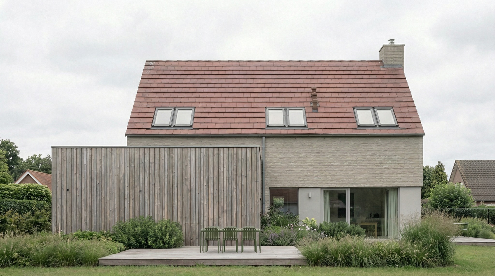 Nowoczesny dom z cegły i drewna z czerwonym dachem. Trzy okna dachowe, drewniany taras z zielonymi krzesłami. Minimalistyczny design, zieleń w otoczeniu.