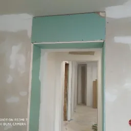 Montaż zielonej płyty gipsowo-kartonowej nad ościeżnicą, ściana w trakcie szpachlowania, widoczne ślady po łatach gipsowych.