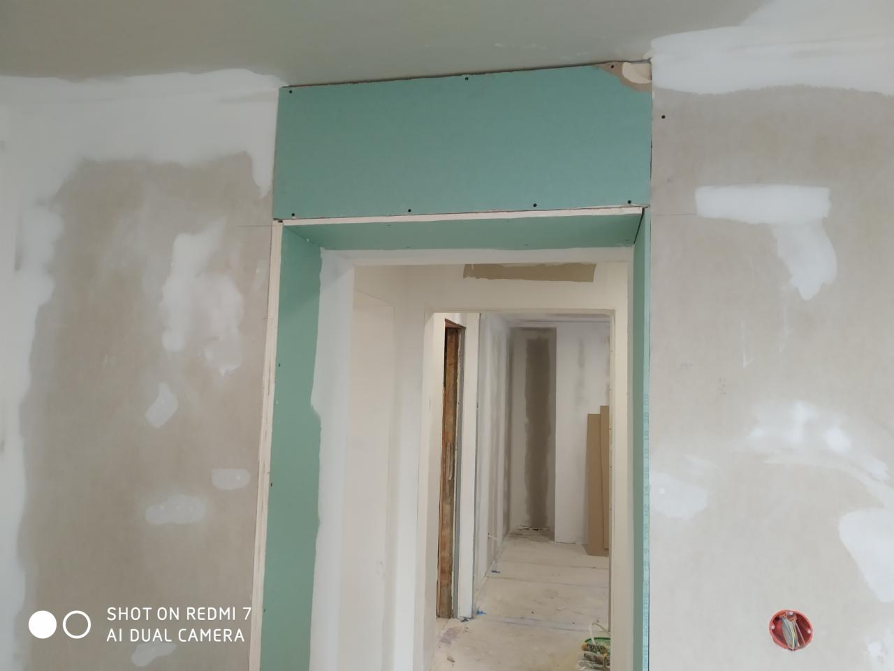 Montaż zielonej płyty gipsowo-kartonowej nad ościeżnicą, ściana w trakcie szpachlowania, widoczne ślady po łatach gipsowych.