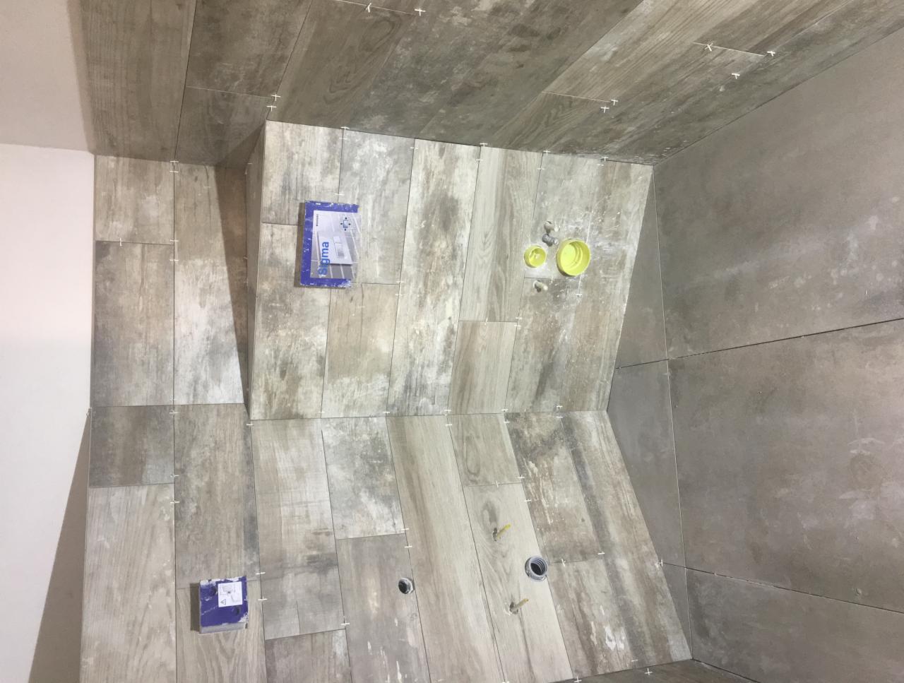 Montaż płytek imitujących drewno w łazience, widoczne krzyżyki dystansowe, puszki instalacyjne i elementy instalacji wodnej.