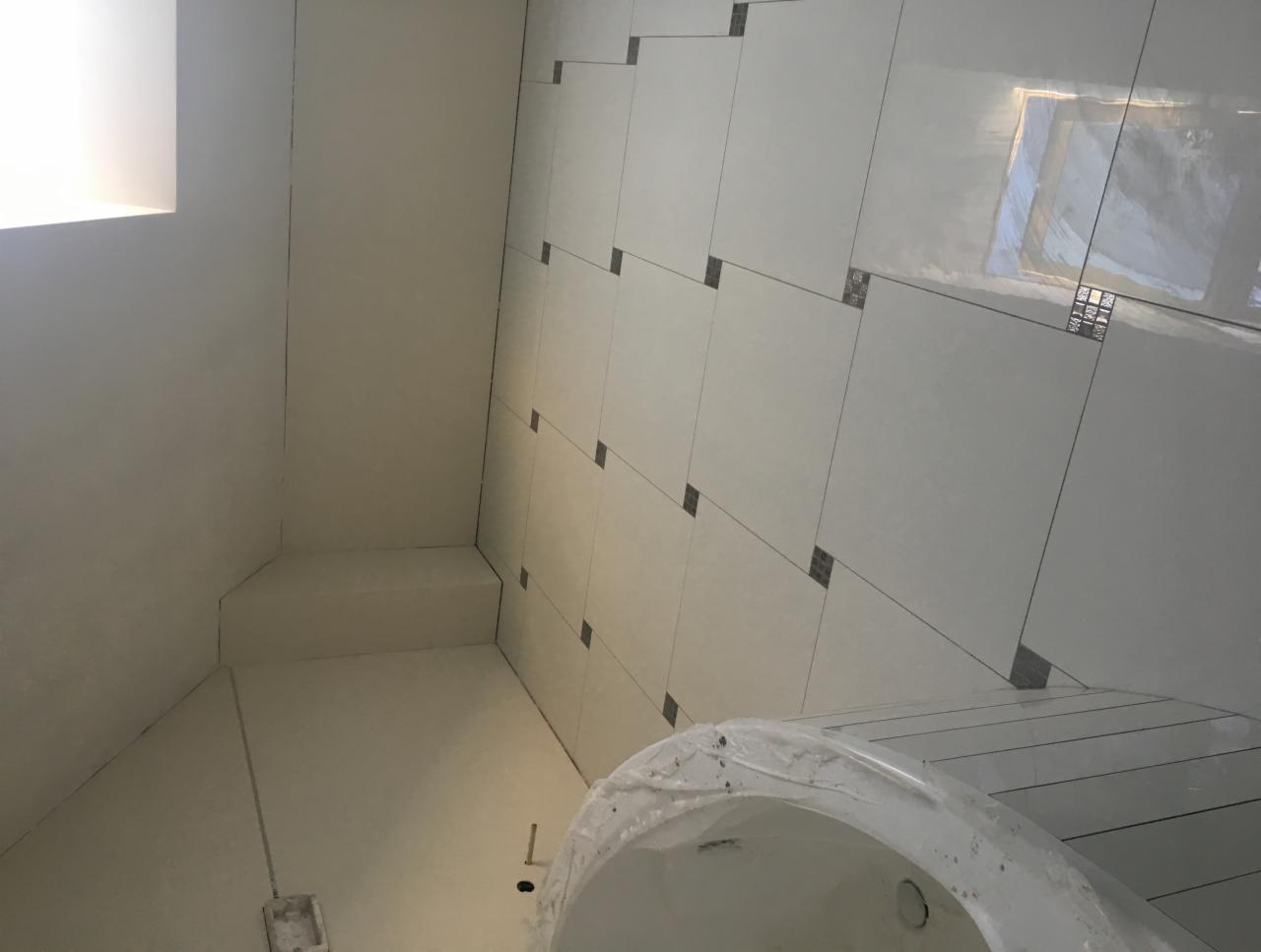 Białe płytki ścienne z dekoracyjnymi wstawkami w narożnikach, częściowo wykończona łazienka z przygotowaną wanną zabezpieczoną folią.