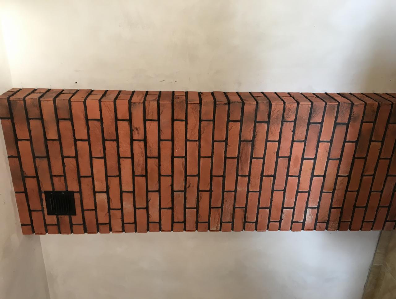 Ceglana obudowa nad kominkiem z kratką wentylacyjną, ściana w surowym stanie przed malowaniem.