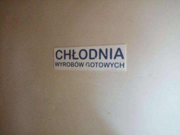 Tabliczka informacyjna z napisem 'Chłodnia wyrobów gotowych' umieszczona na jasnej ścianie.