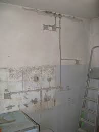 Ściana w trakcie remontu łazienki: widoczne wyprowadzone rury, częściowo położone płytki, surowy tynk i drabina oparta o ścianę.