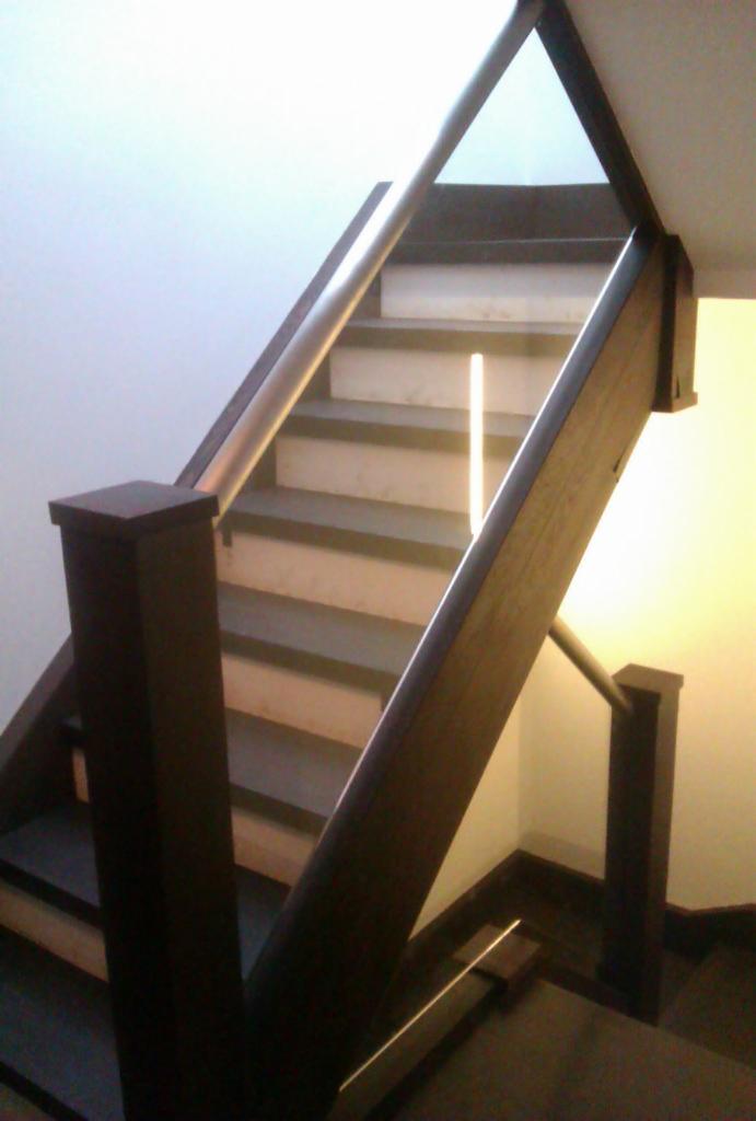 Schody drewniane z metalową poręczą, widok z dołu, z elementami podświetlenia LED na stopniach.