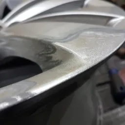 Szlifowanie spawu na metalowym elemencie konstrukcyjnym, widoczne ślady obróbki i narzędzia w tle.