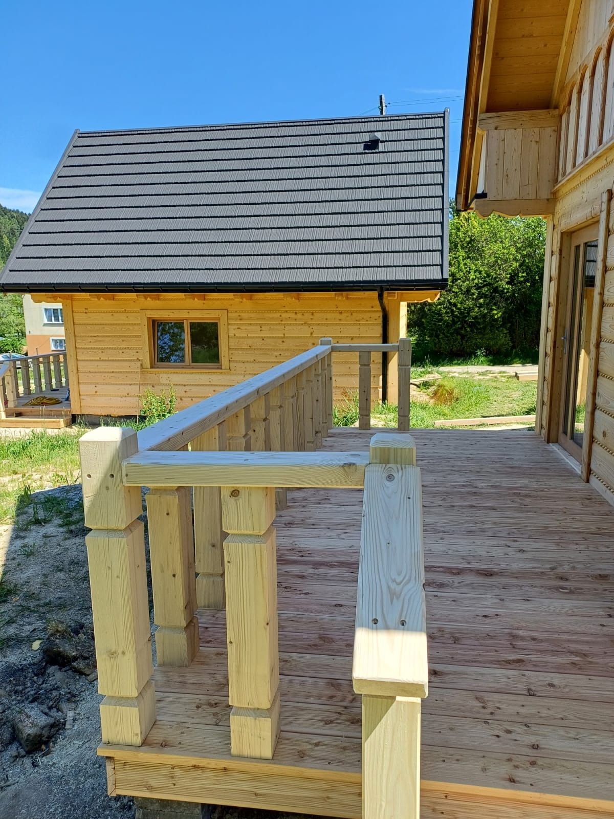 Nowy drewniany taras z balustradą przy domku letniskowym z ciemnoszarą blachodachówką, widok z perspektywy podłogi