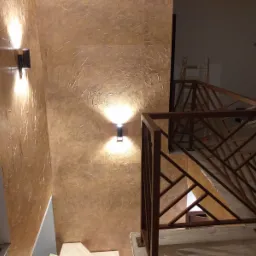 Stiuk wenecki w odcieniach złota, oświetlony kinkietami, widoczny fragment schodów z drewnianą balustradą o geometrycznym wzorze, w tle drabina