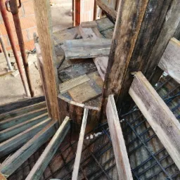 Zbrojenie fundamentu z drewnianym szalunkiem i fragmentami ceglanej ściany w tle, widok z góry.