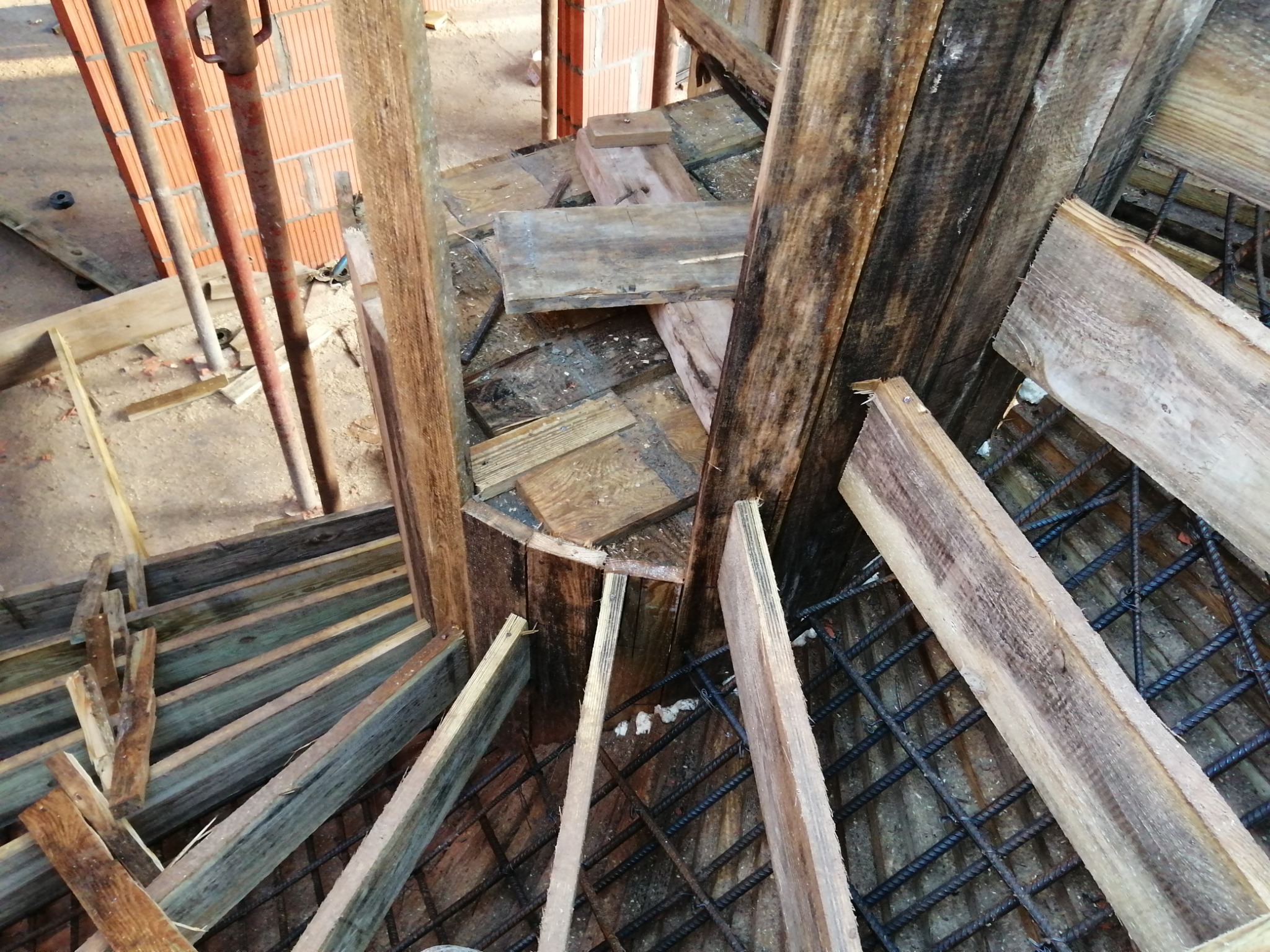 Zbrojenie fundamentu z drewnianym szalunkiem i fragmentami ceglanej ściany w tle, widok z góry.