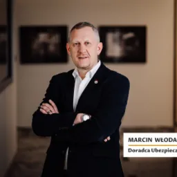 Portret mężczyzny w garniturze, doradcy ubezpieczeniowego Marcina Włodarczyka, na tle korytarza z obrazami.