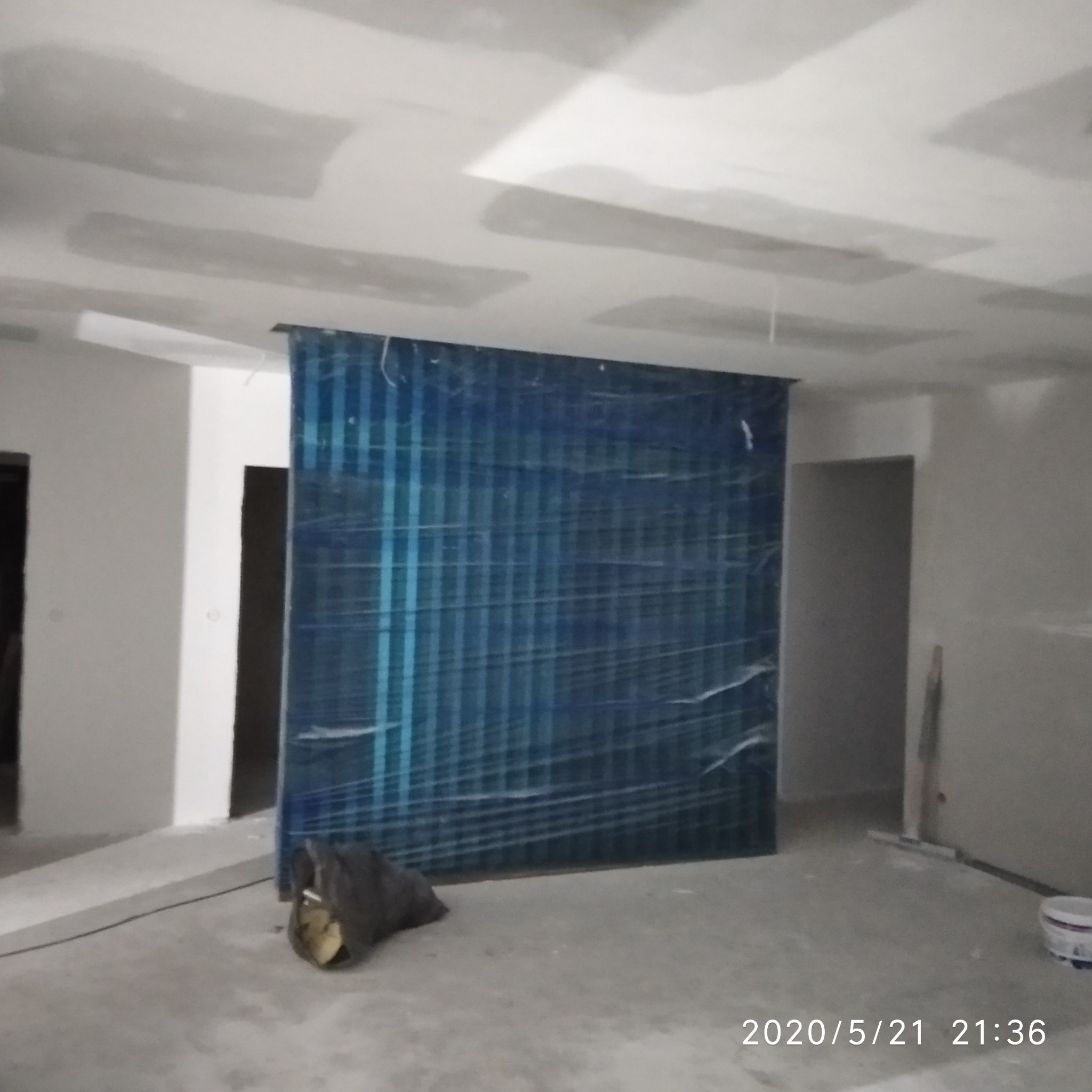 Pokój w trakcie remontu: ściany przygotowane do malowania, zabezpieczona folią ściana z niebieskimi wzorami, widoczne ślady gładzi na suficie, narzędzia malarskie w tle.