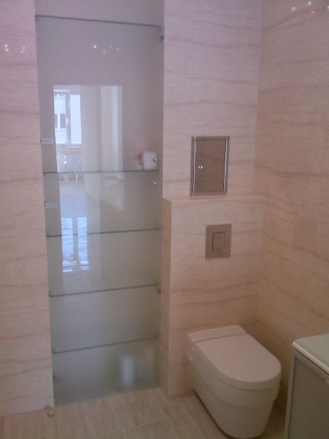 Nowoczesna łazienka z beżowymi płytkami imitującymi marmur, wisząca toaleta, szklana półka w zabudowie i ukryty schowek w ścianie.