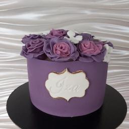 Joanna Stańczak - Fioletowy tort z lukrowanymi różami i napisem 'Iza' na białej etykiecie z obwódką w kolorze starego złota, umieszczony na czarnym podeście.