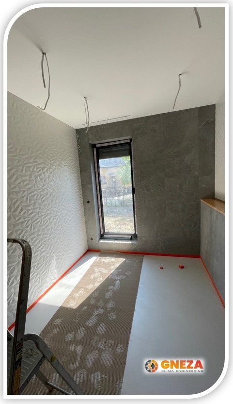 Wnętrze pokoju w trakcie prac instalacyjnych: widoczne wystające kable z sufitu, zabezpieczona podłoga, drabina i logo firmy GNEZA Klima Engineering w rogu.