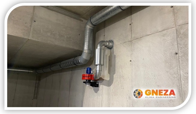 Szare, spiralne rury wentylacyjne zamontowane na surowej, betonowej ścianie, z widocznym czerwonym silnikiem wentylatora i logo firmy Gneza Klima Engineering w prawym dolnym rogu.