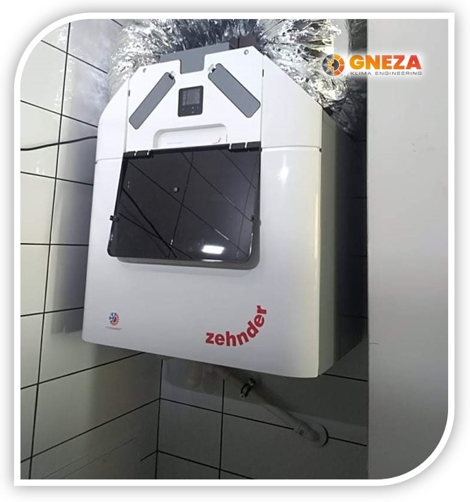 Zamontowane urządzenie wentylacyjne Zehnder z widocznymi przewodami wentylacyjnymi w pomieszczeniu wyłożonym białymi płytkami.