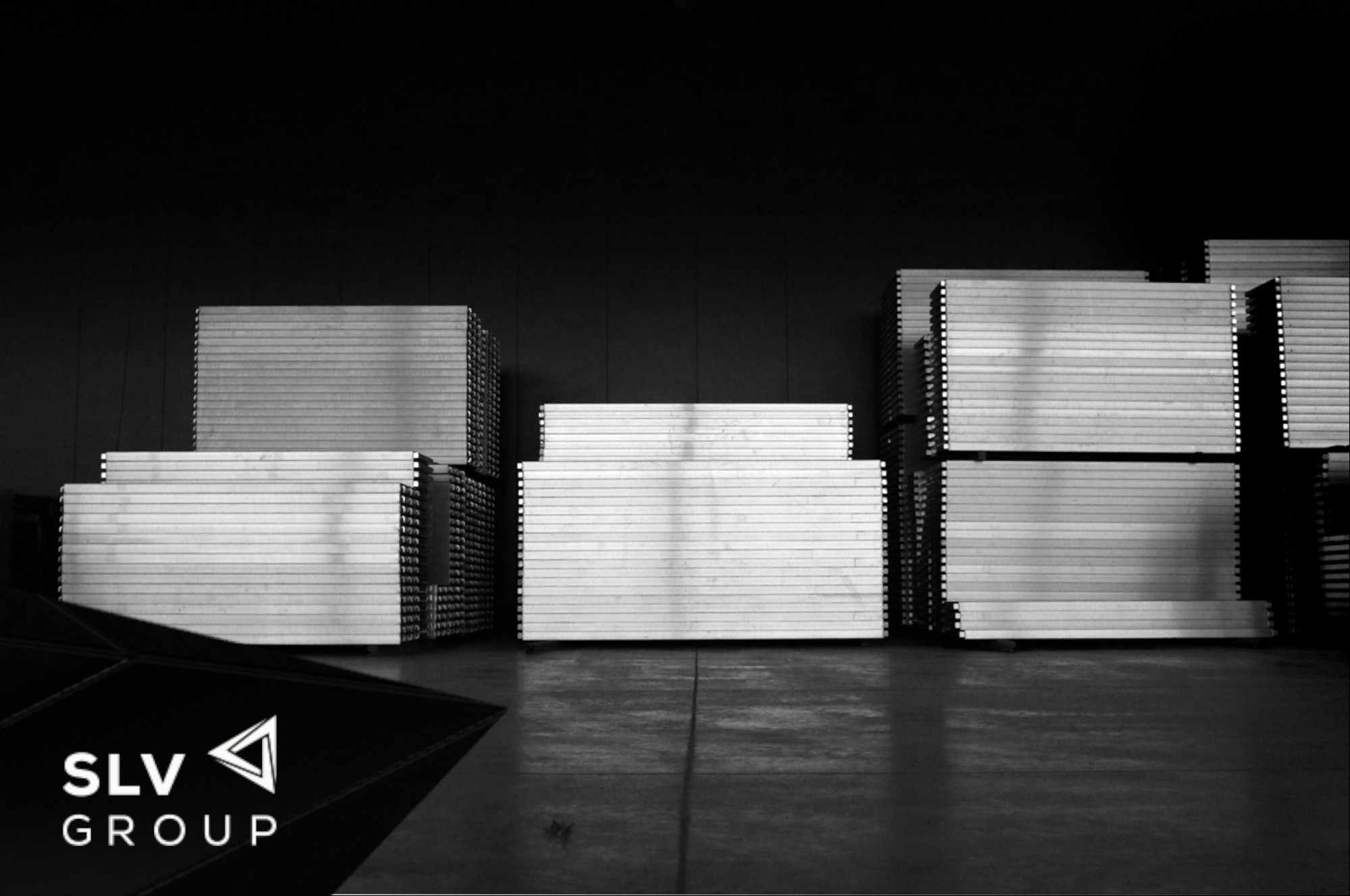 Stosy płyt warstwowych w magazynie, widoczne logo SLV Group w lewym dolnym rogu.