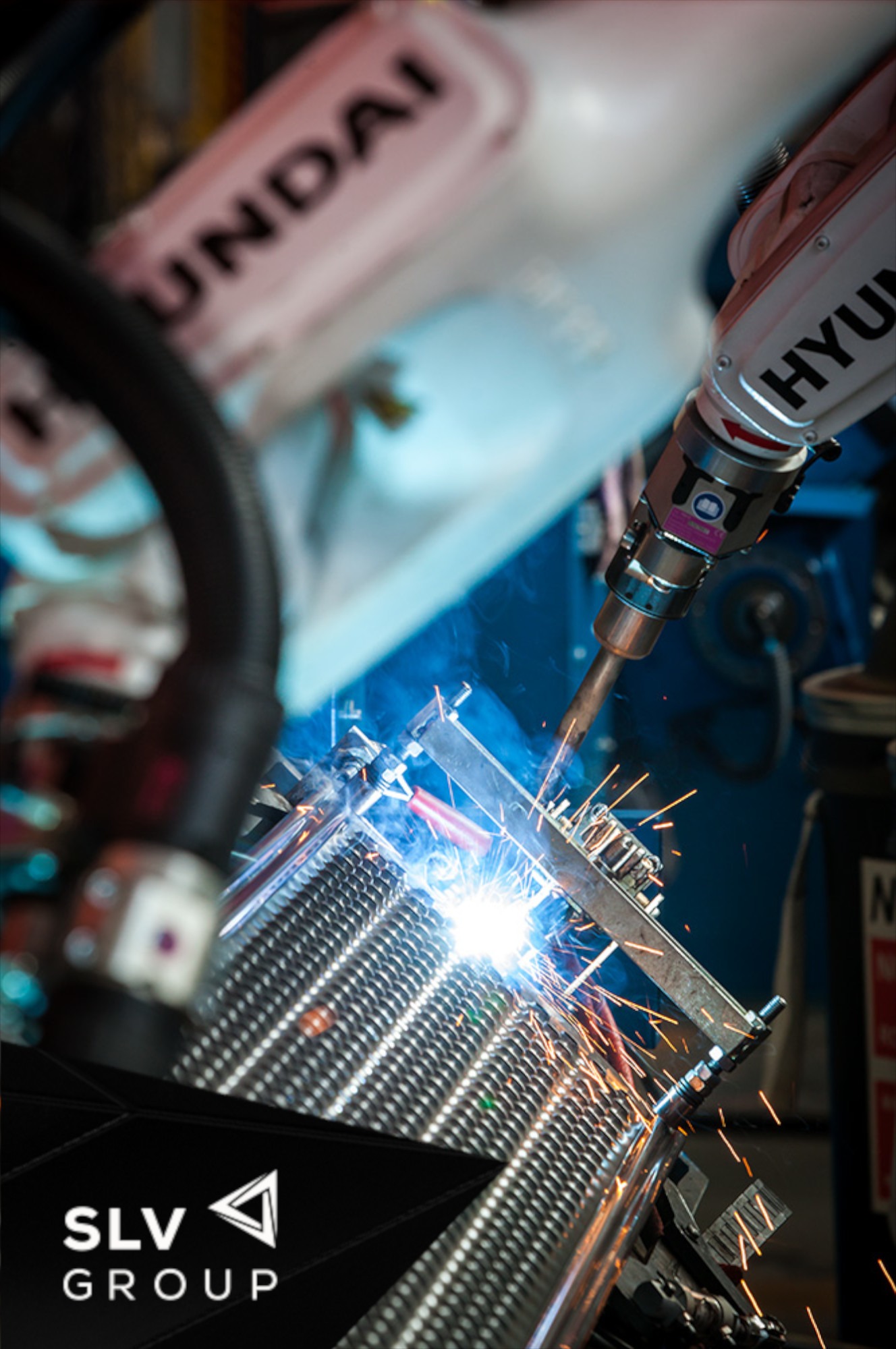 Zautomatyzowane spawanie elementu metalowego za pomocą robotów spawalniczych marki Hyundai, iskry i dym w trakcie pracy.