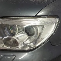 Błyszczący reflektor umytego, szarego samochodu z widocznymi kroplami wody na karoserii.