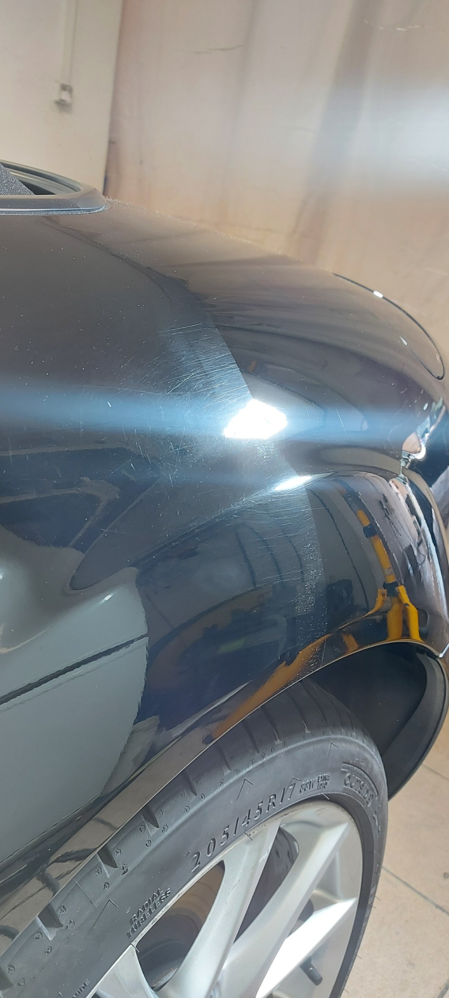 Fragment czarnego samochodu z widocznymi zarysowaniami na błotniku przed myciem, w tle widoczna opona z felgą.