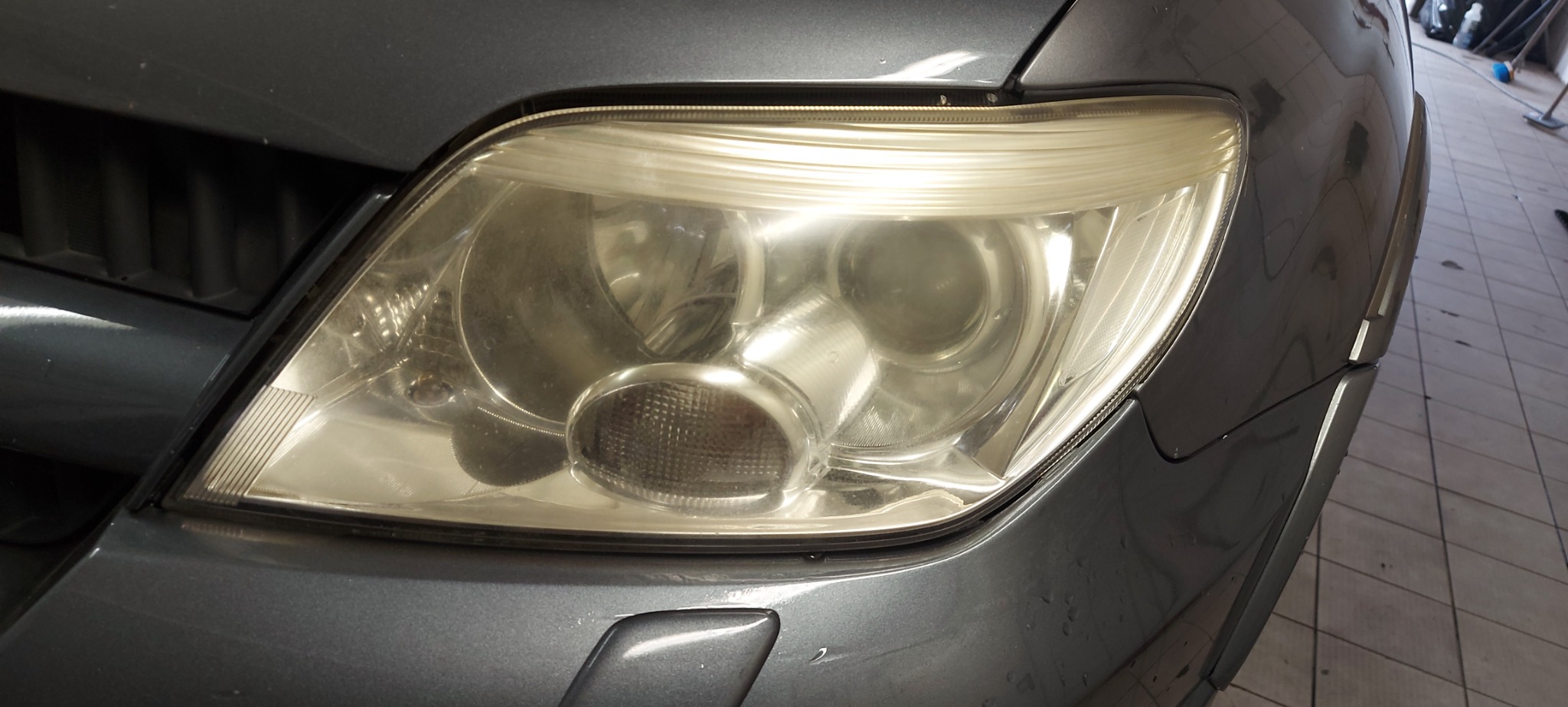 Prawy reflektor samochodu w kolorze grafitowym przed czyszczeniem, widoczne zarysowania i zamglenia na kloszu.